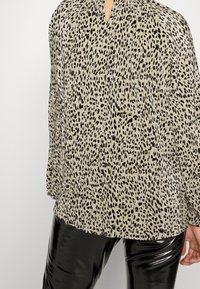 Top beige plissettato con motivo a stampa leopardata nera, presenta un scollo a V e maniche lunghe; abbinato a leggings neri lucidi.