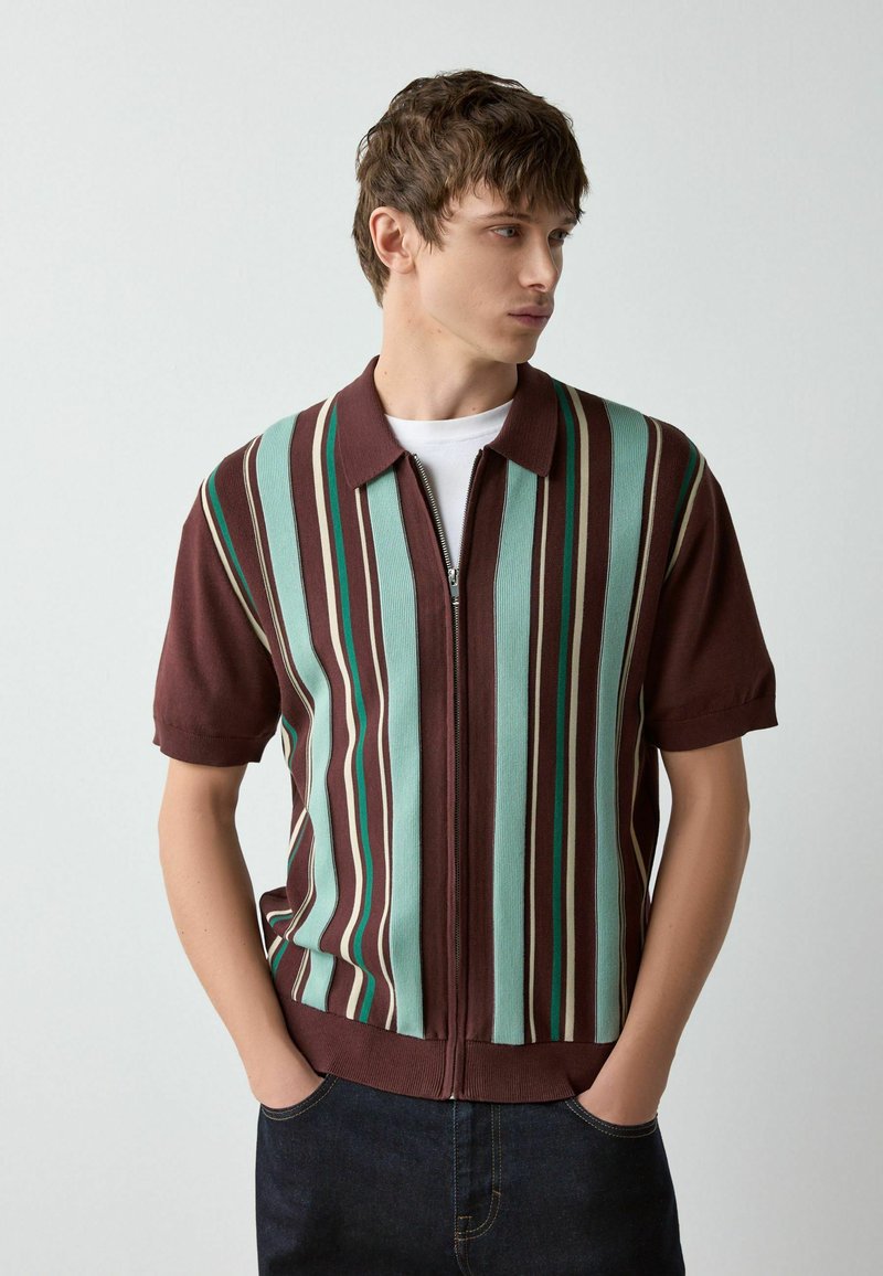 Lühikeste varrukatega pruun lukuga särk, millel on vertikaalsed triibud mündirohelises ja-kreemjas toonis. Pehme tekstuur, soonikuga kangas, klassikalise krae kujundus.