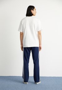 White cotton T-shirt with short sleeves, paired with navy blue pants featuring white side stripes. Displayed from the back.