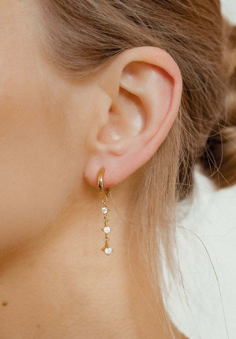Boucle d'oreille en or avec une délicate chaîne pendante ornée de quatre petites pierres précieuses, présentant une finition brillante et un design élaboré.
