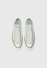 Light blue canvas sneakers with white laces, cream toe cap, and black accenting. Gold eyelets adorn the lace holes. Non-slip outsole.