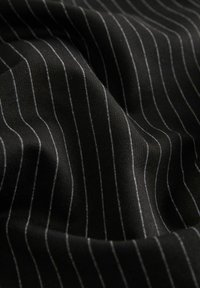 Svart tyg med tunna vertikala vita ränder, som visar en mjuk textur och draperade veck, vilket framhäver mönstret och färgkontrasten.