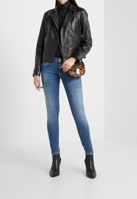 Giacca di pelle nera da motociclista, dolcevita nera aderente, jeans skinny blu, stivali neri alla caviglia e borsa a tracolla con stampa leopardata.