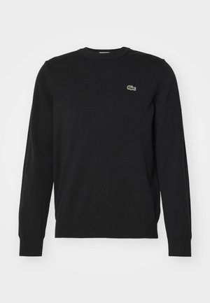 Czarny sweter crewneck wykonany z dzianiny, z prążkowanymi mankietami i dołem. Posiada małe, zielone wyszywane logo krokodyla na klatce piersiowej.