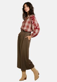 Rood geruit blouse met geborduurde bloemenaccenten, gecombineerd met hoge bruine broeken en beige hakken.