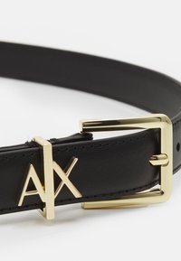 Juodas odinis diržas su blizgia auksine stačiakampio formos sagtimi ir "AX" logotipu. Diržas yra paprastas, su matomomis siūlėmis ir reguliuojamais skylutėmis.