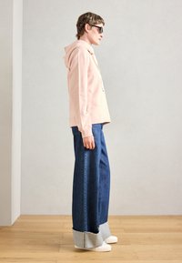 Felpa con cappuccio rosa chiaro dal fit rilassato, abbinata a jeans a gamba larga blu scuro con orlo grezzo e polsini in denim blu chiaro. Sneakers bianche.