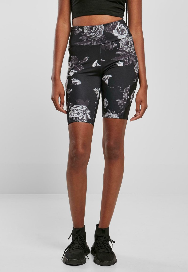 Shorts de vélo taille haute à motif floral noir, avec une texture lisse et une coupe mi-genoux, associés à des chaussures de sport noires.