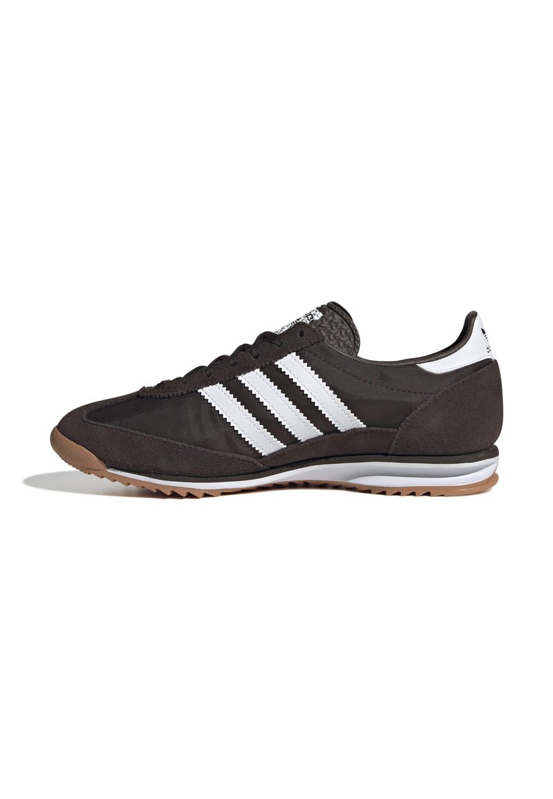 Chaussure de sport noire en daim et matériaux synthétiques avec trois rayures blanches, semelle en caoutchouc et détails texturés au niveau du talon.