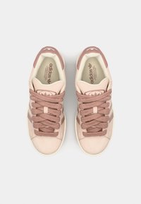 Růžové semišové tenisky s tmavšími růžovými akcenty. Mají silné tkaničky a design se třemi pruhy. Měkká látková podšívka a logo na jazyku.