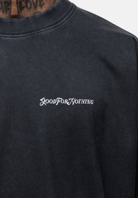 Czarny sweter z miękkiego materiału, z okrągłym dekoltem. Z przodu znajduje się tekst "GOOD FOR NOTHING" w białym, kursywnym stylu.