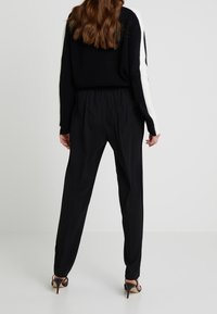 Pull en maille noir avec des rayures blanches contrastantes sur les manches, associé à un pantalon noir ample et des escarpins noirs à talons aiguilles.