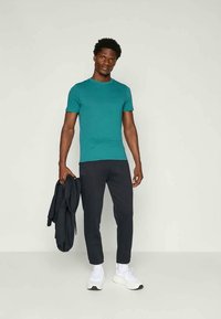 Τυρκουάζ κοντομάνικο t-shirt σε συνδυασμό με σκούρες φόρμες, λευκά αθλητικά παπούτσια και ένα μαύρο μπουφάν κρατημένο χαλαρά στο ένα χέρι. Απλός σχεδιασμός και εφαρμογή.