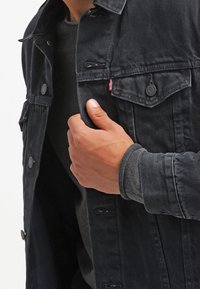 Veste en jean bleu marine foncé au style classique, avec des boutons pression en métal, des poches sur la poitrine et une texture subtile. Agrémentée d'une étiquette de marque.