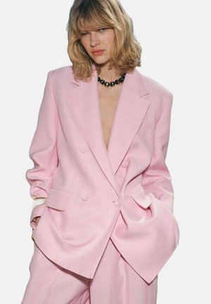 Blazer rose à double boutonnage avec revers crantés, épaules larges et poches latérales ; fabriqué à partir d'un tissu lisse et structuré.