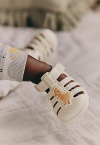 White, rubber baby sandals with cut-out design and a duckling accent, featuring adjustable strap and textured sole.