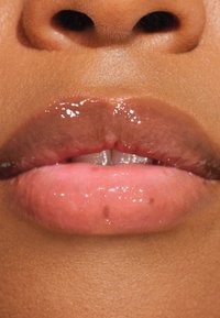 Labbra lucide e piene con un gradiente che va dal rosa tenue a un marrone più scuro. Struttura liscia con una leggera lucentezza e variazioni di colore naturali.