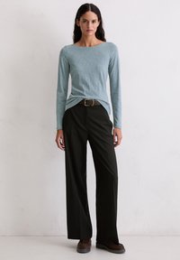 Gai zilo garām piedurknēm topu ar apaļu kakla izgriezumu, saskaņots ar augsta josta platām melnām biksēm, papildināts ar brūnu jostu un apaviem.