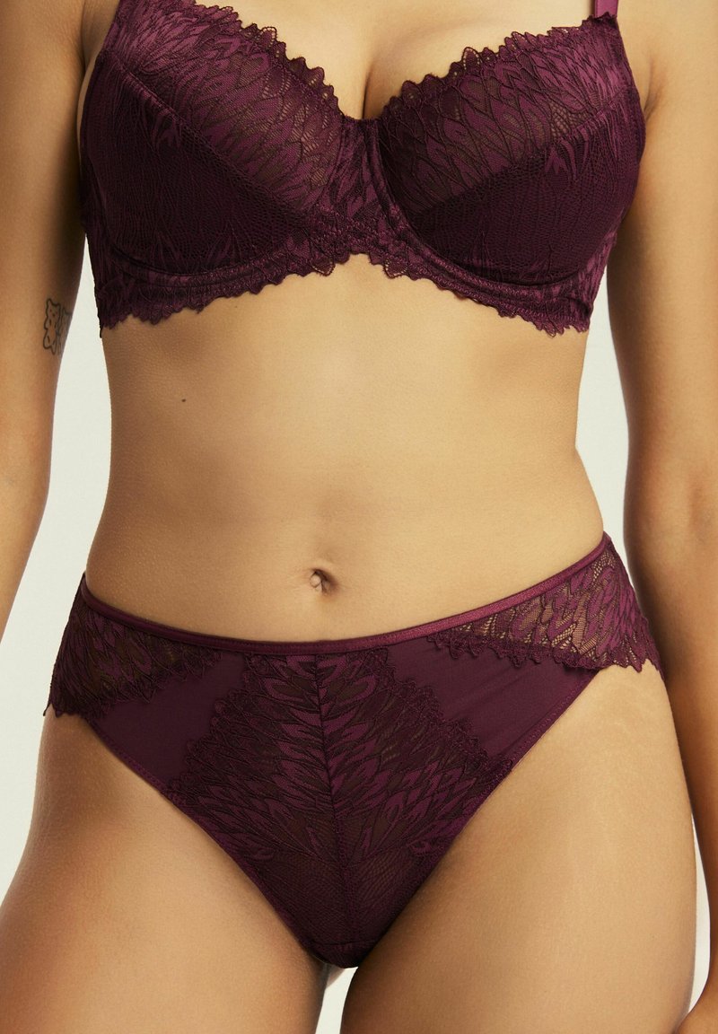 Bordowy koronkowy biustonosz balkonowy i pasujące figi z wysokim stanem. Posiada falbaniaste krawędzie i misternie wykonane kwiatowe wzory na przezroczystym materiale.