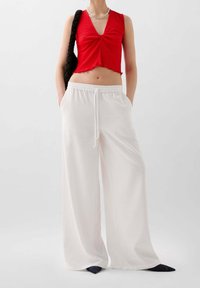 Rød cropped top med V-hals og flæset kant, parret med løse hvide bukser med elastisk talje og sidelommer.