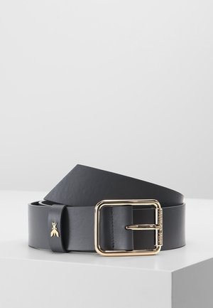 Zwarte lederen riem met een gouden vierkante gesp en een klein gouden insectenembleem op de riemlus, liggend op een witte ondergrond.