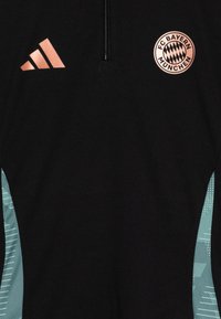 Musta urheilullinen vetoketjukauluksellinen pusero, jossa on vaaleansininen geometrinen sivukuosi ja näkyvä FC Bayern Münchenin logo bronssinvärisenä.