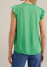 Zielony krótki top z krótkim rękawem, ozdobiony falbankami na ramionach i okrągłym dekoltem. Wykonany z lekkiego materiału o gładkiej teksturze z zaokrąglonym dołem.