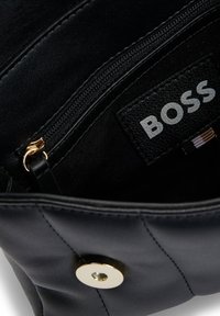 Black leather handbag interior featuring a zip pocket and a tag with "BOSS" logo. Gold hardware detail and smooth texture.