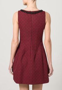 Robe rouge avec un corsage ajusté et une jupe évasée, ornée d'un col en perles noires. Présente un motif texturé sur l'ensemble.