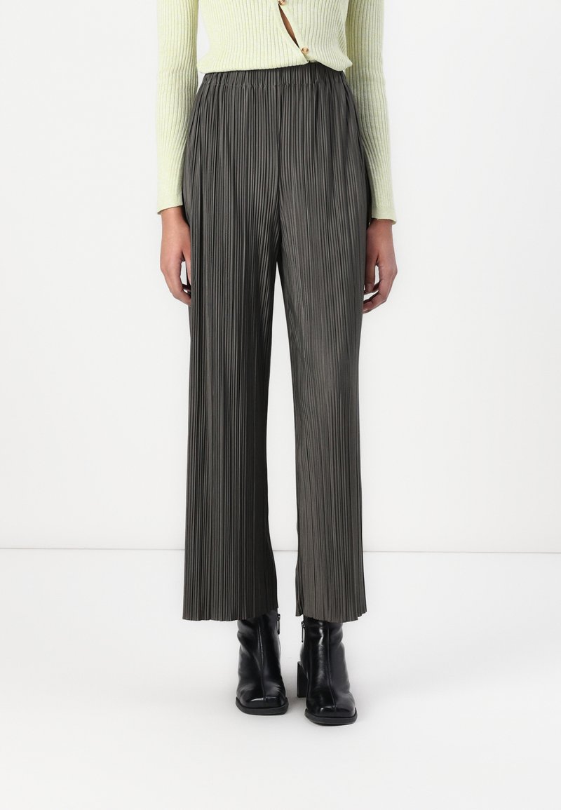Pantalons plissés vert foncé avec une coupe large et une taille élastique, associés à des bottines noires. Le tissu texturé crée de la profondeur.