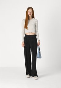 haut court blanc à côtes avec bords effilochés, pantalon large plissé noir, et sac à épaule bleu clair, associé à des baskets grises.