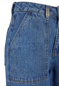 Gros plan sur un jean en denim bleu montrant la poche avant, la boucle de ceinture avec une étiquette métallique et les coutures détaillées sur le tissu.