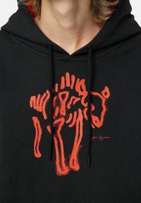 Felpa nera con cappuccio dotata di una grafica astratta rossa e audace di un orso. Design semplice con cappuccio regolabile e texture in cotone morbido.