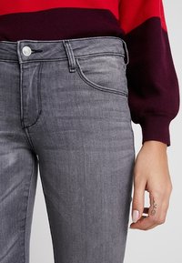 Jeans de mezclilla gris con una textura suave, diseño de cinco bolsillos y cierre de botón. La cinturilla tiene un detalle de costura visible.