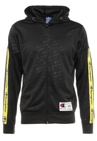 Svart zip-up hoodie med ett texturerat mönster, med en kontrasterande gul rand på ärmen, logoprydnader och justerbar dragsko på huvan.