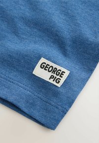 Kék pamut anyag sima felülettel; egy fehér címke található rajta, amelyen feketével van nyomtatva a "GEORGE PIG" felirat. Az élen varrási részlet látható.