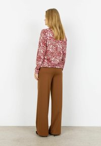 Dlhý rukáv, top s kvetinovým vzorom v červených a ružových tónoch s voľným strihom, kombinovaný so širokými hnedými nohavicami, zobrazený zozadu.