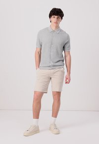 Polo tricotat gri cu mânecă scurtă, cu un design texturat, cu deschidere cu nasturi, asortat cu pantaloni scurți bej și adidași albi.