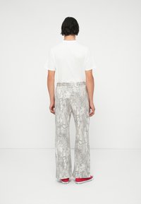 Gray patterned wide-leg pants with an elastic waistband, paired with a white t-shirt and red sneakers, viewed from the back.