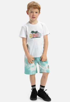 Bílý tričko s logem "Quiksilver" a palmami, spárováno s mátovými tie-dye šortkami. Černé tenisky s bílými a černými pruhovanými ponožkami.