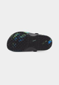 Μαύρη σόλα παπουτσιού με πέλμα σε σχήμα αστεριού, διακοσμημένη με μπλε και πράσινα πινελιές χρώματος στα σημεία της φτέρνας και της μύτης, σε λευκό φόντο.