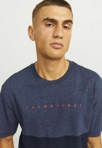 Tamsiai mėlyna trumpomis rankovėmis marškinėliai su raudonu "JACK & JONES" logotipu. Pagaminti iš tekstūruotos medžiagos su kontrastinga tamsiai mėlyna apatine dalimi.
