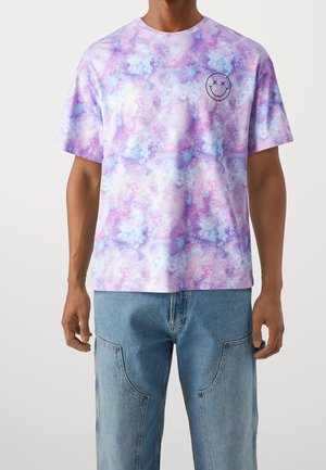 T-shirt graphique en tie-dye violet et bleu clair avec un motif de smiley sur la poitrine gauche. Coupe décontractée et en matière coton.