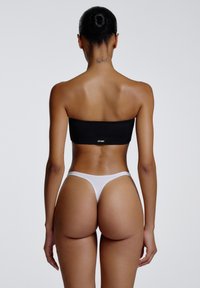 Haut noir sans bretelles et string blanc, tissu sans couture, coupe ajustée, et branding minimaliste sur le haut. Texture lisse, couleurs neutres.