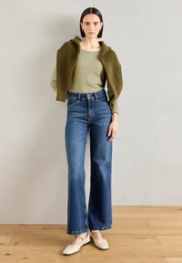 Olivenfarget langermet topp under en stripete strikket cardigan, kombinert med høymidjer blå vide jeans og beige flate sko.