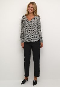 Blusa a righe bianco e nero con scollo a V, maniche lunghe e polsini elastici, abbinata a pantaloni neri e mules con tacco.