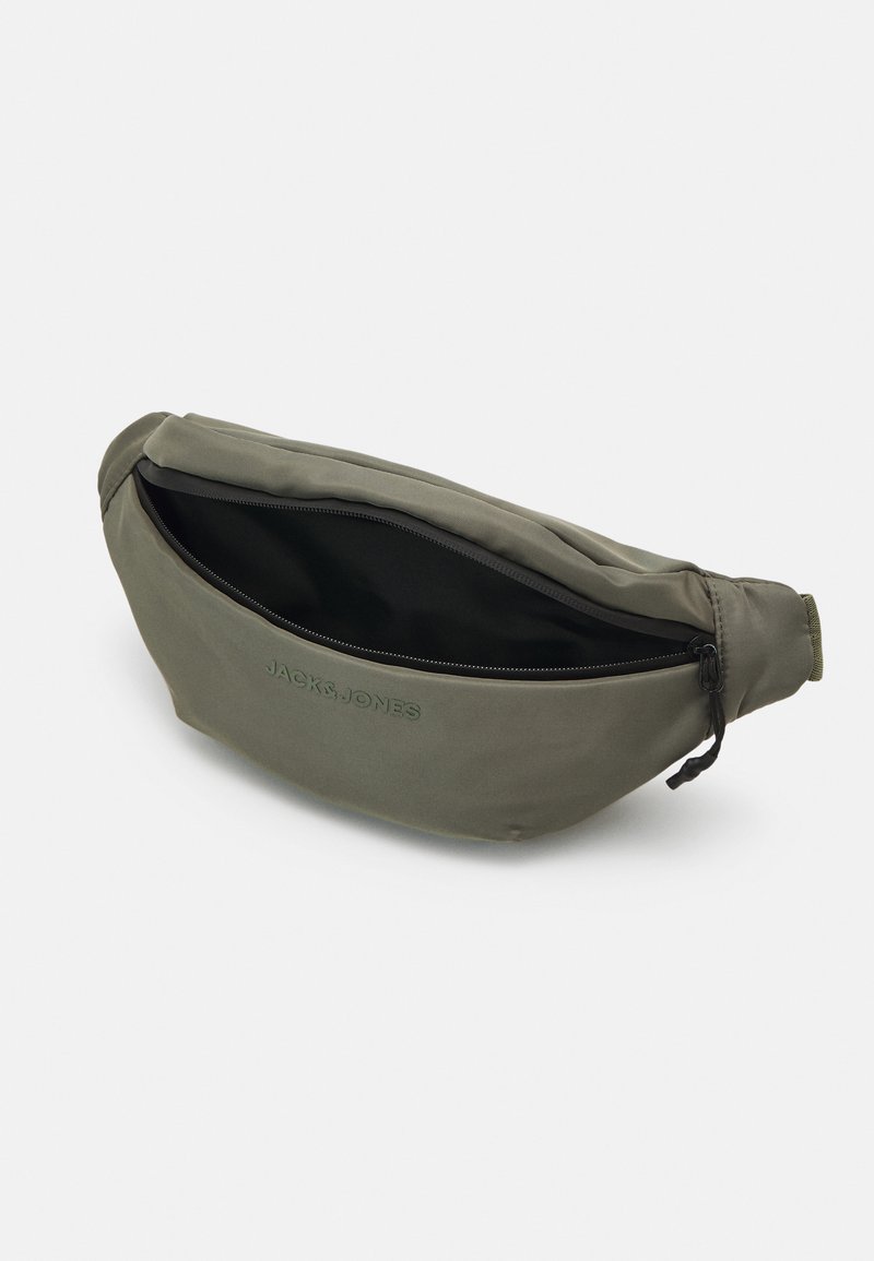 Riñonera de color verde oliva hecha de tela texturizada, con cierre de cremallera, logotipo en relieve y una forma delgada y redondeada. El interior es negro.