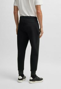 Svarta joggers med elastiskt midjeband, manschetterade fållar och en bakficka. Slät textur och minimalistisk design. Matcher med svarta sneakers.