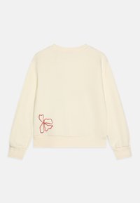 Sweat-shirt crème à manches longues, avec des poignets côtelés et un col légèrement rond. Présente un motif floral rouge brodé dans le dos.
