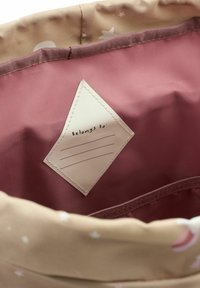 Interiorul rucsacului din pânză, în roz și bej deschis, prevăzut cu o etichetă pentru personalizare. Decorat cu stele și luni albe.